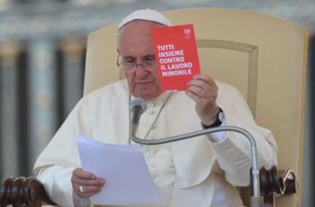 Papa Francisco está sentado e segurando, com a mão direita uma carta, e com a esquerda, um cartão vermelho contra o trabalho infantil