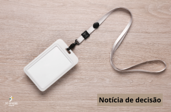 crachá de identificação sobre uma mesa de madeira. À esquerda da tela, a assinatura do TRT-15. À direita, os dizeres: Noticia de decisão, em preto.