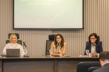#ParaTodosVerem: três mulheres sentadas em cadeiras pretas atrás de uma mesa de madeira