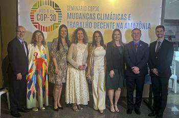 oito pessoas posam em pé para foto com um banner do evento da Cop 30 atrás