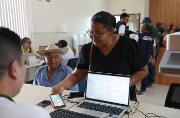 Senhora é atendida em guichê da Justiça do Trabalho por um homem que está em frente a um notebook