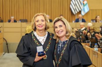 Dra. Tereza posa para foto segurando a medalha, ao lado da Dra. Ana Paula 