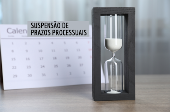 calendário e ampulheta sobre a mesa com o texto Prazos Processuais em preto, num retângulo cinza