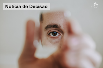 quadro cinza com homem que segura um pequeno espelho com as mãos desfocadas, que exibe um de seus olhos