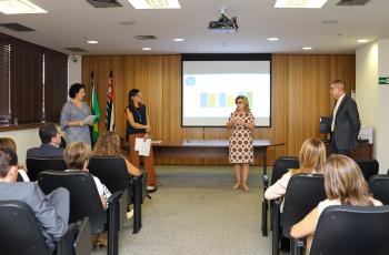 #ParaTodosVerem: três mulheres e um homem estão de pé, sendo observados por um pequeno público sentado em cadeiras pretas