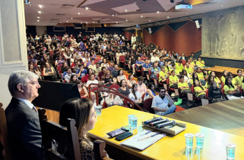 plateia ao fundo com o Dr. Pelegrini e Dra. Marina em primeiro plano, do lado esquerdo, sentados à mesa