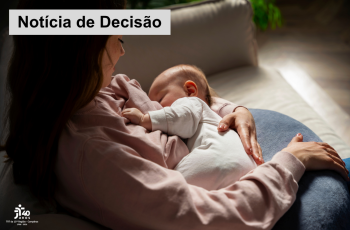 Mulher de blusa rosa está sentada no sofá amamentando um bebê