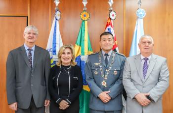 Homenageado possa para foto ao lado dos desembargadores Edison Pelegrini, Ana Paula e Helcio Dantas em frente a uma parede de madeira e quatro bandeiras
