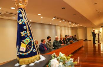 #ParaTodosVerem: mesa de honra com integrantes sentados. à frente, à esquerda, a imagem de Nossa Senhora Aparecida.