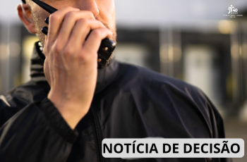 Imagem em close mostra parte do rosto e do tronco de um vigilante uniformizado, utilizando um rádio comunicador junto ao rosto. O fundo está desfocado, sugerindo um ambiente corporativo ou comercial. No canto inferior direito, há a inscrição "Notícia de Decisão" e, no canto superior direito, a marca comemorativa dos 40 anos do TRT da 15ª Região.