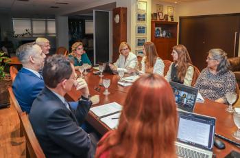 Pessoas sentada em volta de uma mesa oval participam de uma reunião.