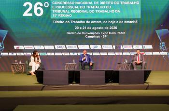 palestrantes e mediador no palco sentados em poltronas, com telão sobre o congresso ao fundo