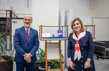 Um homem e uma mulher posam para a foto ao lado de uma caixa onde estão em exposição um selo e uma moeda comemorativa dos 40 anos do TRT 15.
