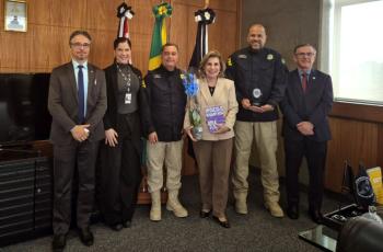foto posada com Dra. Ana Paula, segurando um livro e uma orquídea, com o assessor Cleber, Dr. João e três representantes da PRF, sendo uma mulher