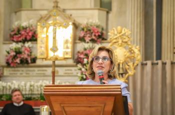 Dra. Ana Paula está no púlpito fazendo a leitura da Carta. Ao fundo, o nicho de Nossa Senhora Aparecida